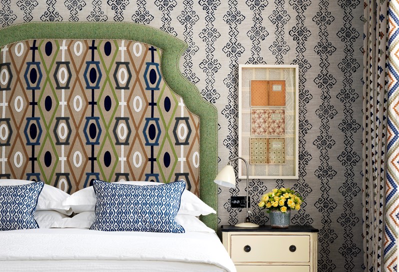 A detail of the headboard, with a graphic beige design against a pale green trimming. Next to the bed is a cream bedside table with a small lamp.
