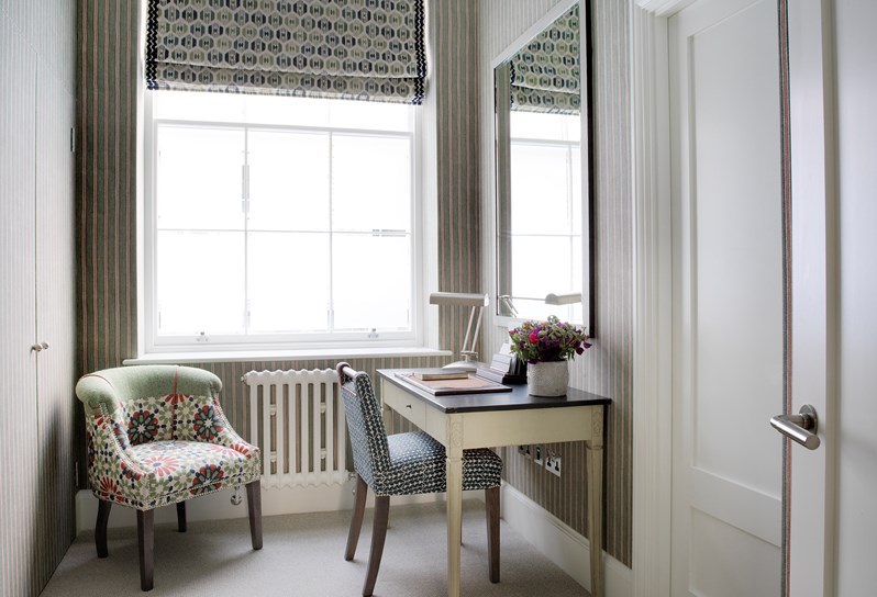 The bright dressing room at Haymarket Hotel, featuring a writing desk and a small armchair set against striped wallpaper.