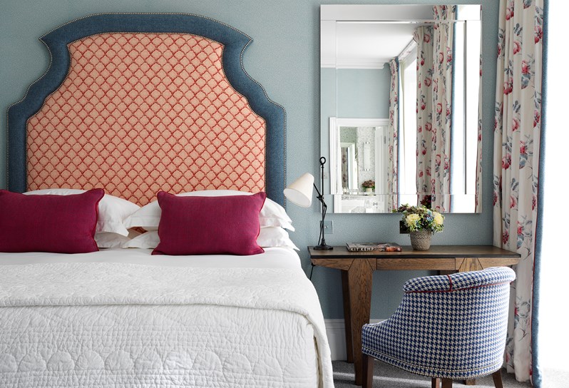 A double bed with an ornate red patterned headboard with blue trimming set against a pale blue wall.