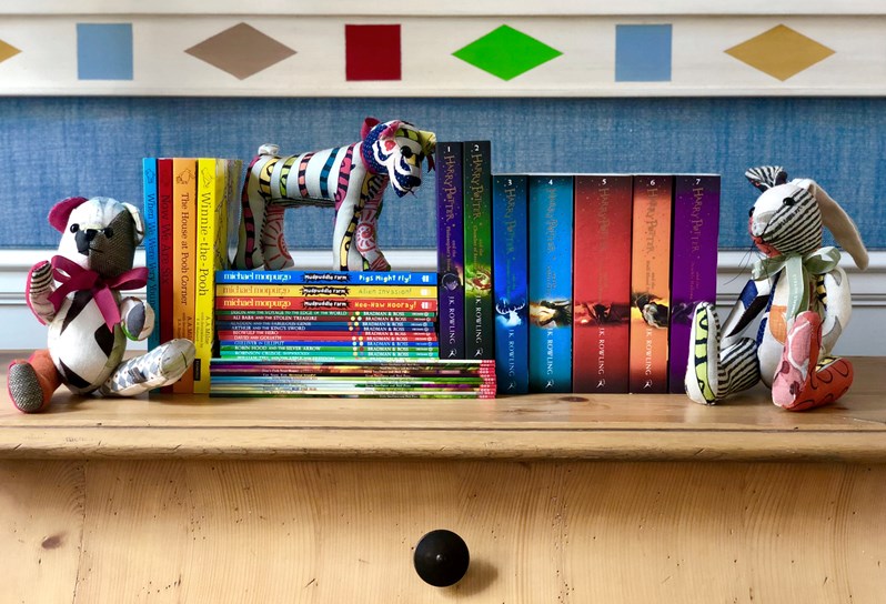 A collection of childrens book on a wooden shelf surrounded by childrens toys