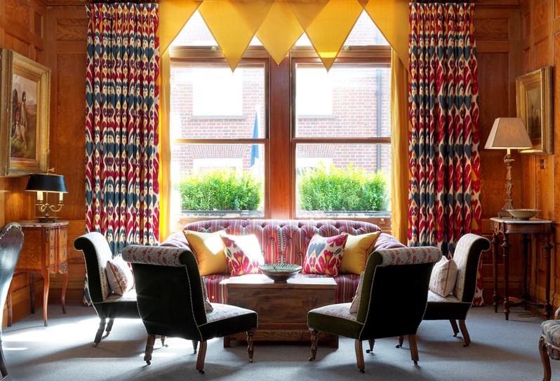 A sunny wood panelled drawing room with yellow curtains above a striped sofa