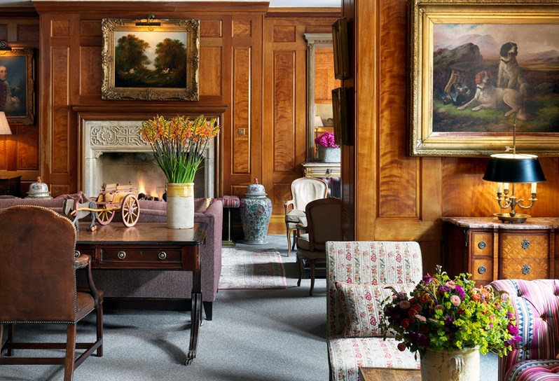 Drawing Room at Covent Garden Hotel with wooden wall panels and a fireplace set as a lounge set up with sofas and comfy chairs over Persian rugs