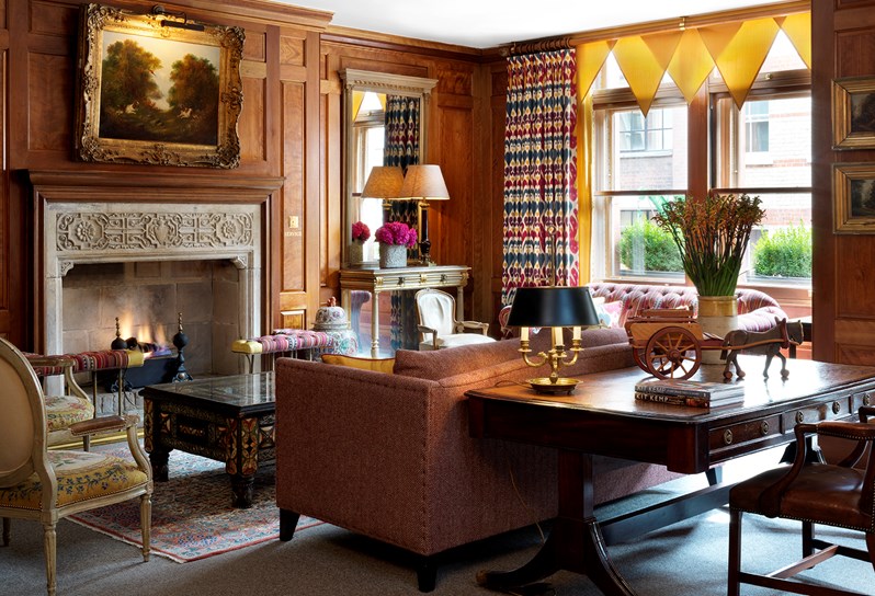 Drawing Room at Covent Garden Hotel with wooden wall panels and a fireplace set as a lounge set up with sofas and comfy chairs over Persian rugs