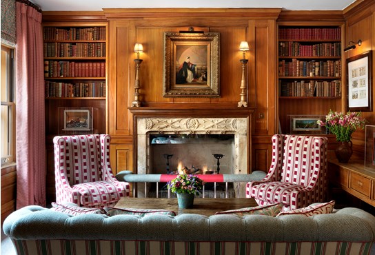 The wood panelled library with open fireplace and red arm chairs