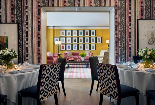 The Covent Garden Hotel Fortune function room with a striped wallpaper and a black table laid for dinner in the foreground. Open double doors look through the bright yellow Lyric room.