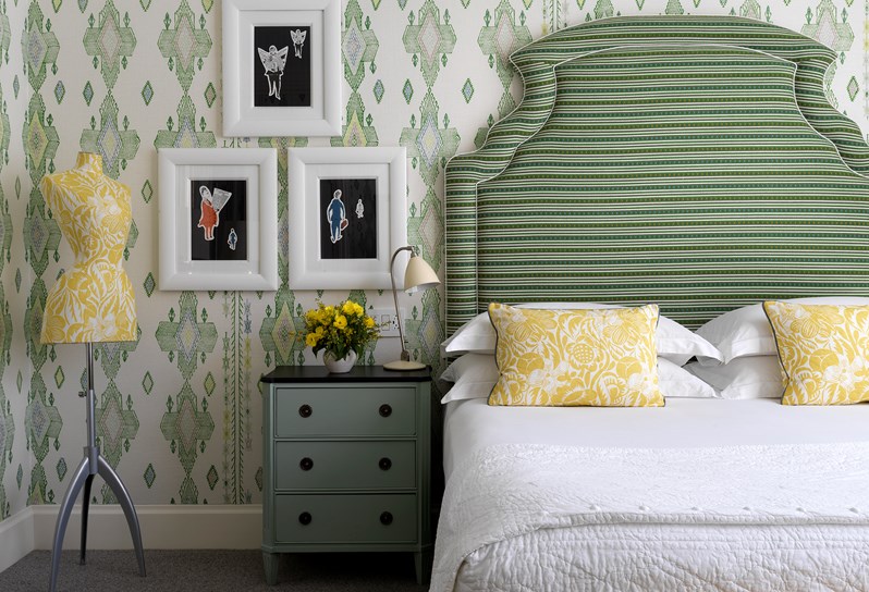 A spacious bedroom with walls lined in an green ikat pattern. This is a large king size bed with a green statement headboard. At the back of the room is floor to ceiling crittal windows.