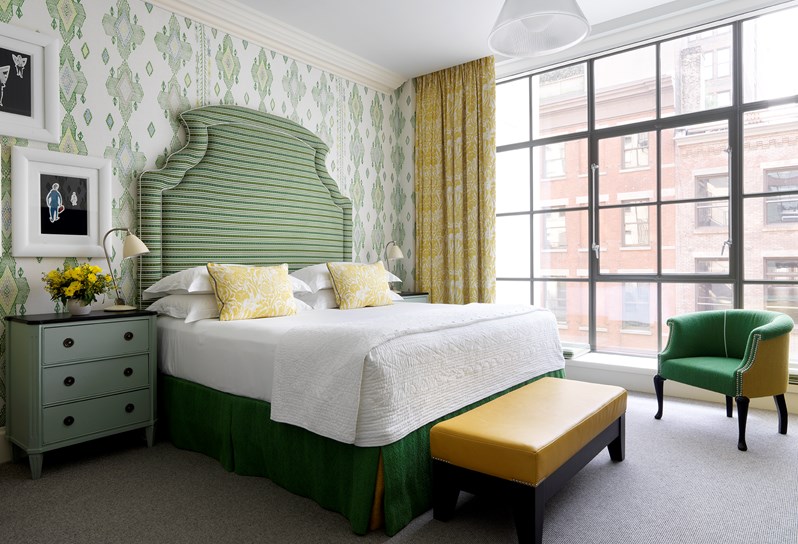 A spacious bedroom with walls lined in an green ikat pattern. This is a large king size bed with a green statement headboard. At the back of the room is floor to ceiling crittal windows.