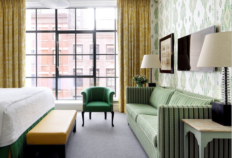 A spacious bedroom with walls lined in an green ikat pattern and yellow curtains surrounding the floor to ceiling crittal windows.