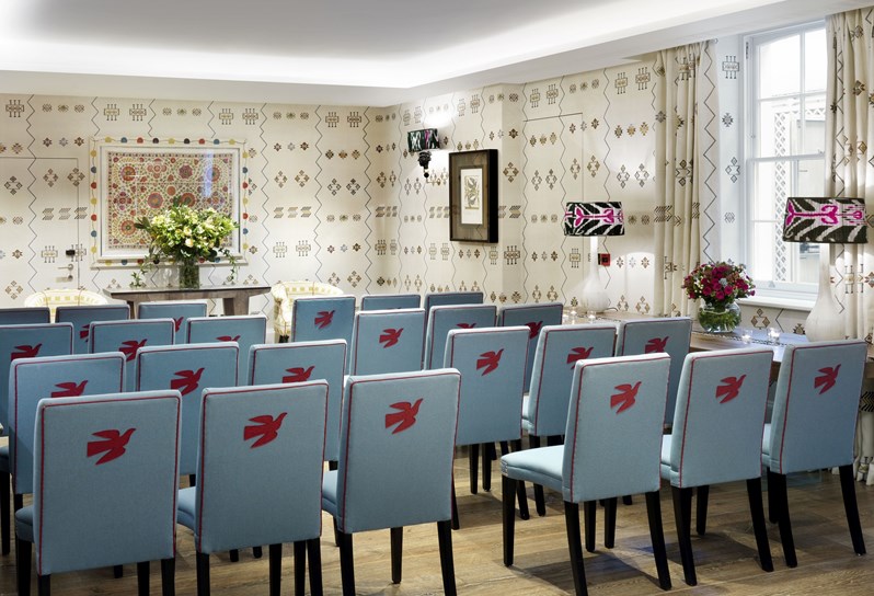 Blue chairs in rows ceremony style facing towards the back of the room. The room has cream printed wallpaper.