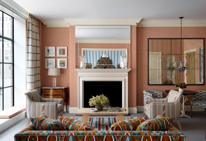 The living room with fresh flowers in a one bedroom suite at the Crosby Street Hotel with terracotta colour scheme with a cream striped sofa in front of floor length windows with views of the SoHo neighbourhood.