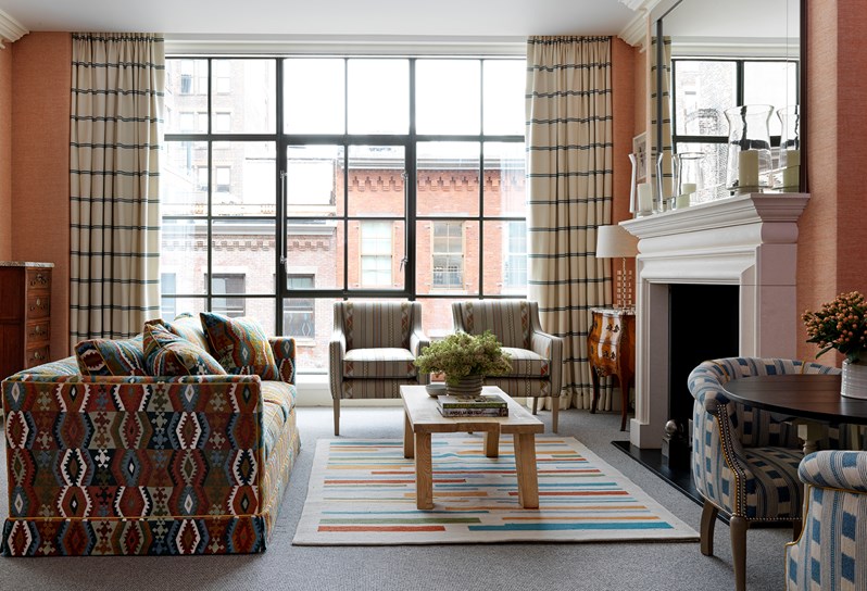The living room with fresh flowers in a one bedroom suite at the Crosby Street Hotel with terracotta colour scheme and floor length windows with views of the SoHo neighbourhood.