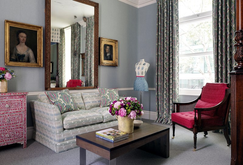 A view of a living space with a sofa and armchair framing a coffee table. The room has blue walls and a large window which floods the room with natural light.