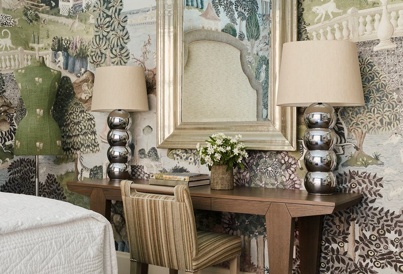 A writing desk is set against a wall with a hand painted wallpaper depicting green rolling hills with trees and creatures.