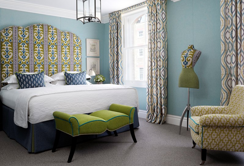 A spacious bedroom with bright blue walls and a king size bed with a blue and green fabric headboard