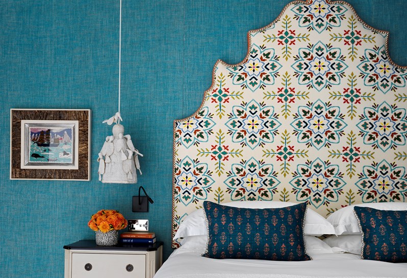 A bedroom with vibrant blue linen walls and a white patterned headboard