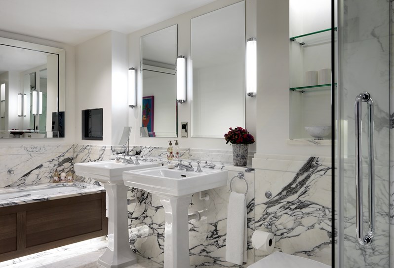 A modern bathroom with white marble on the walls and two sinks infront of a mirror