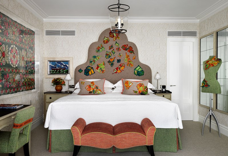 A bedroom with white fabric walls. The bed has a tall statement headboard with intricately embroidered oak leaves.