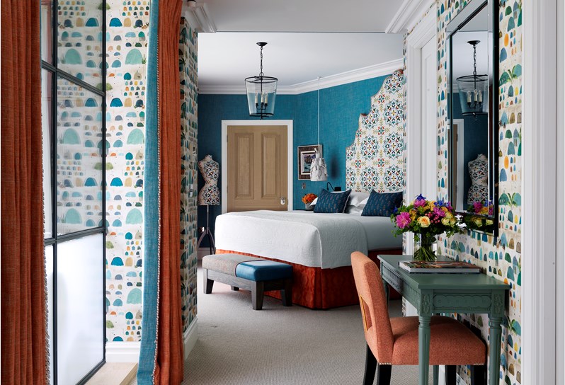 Looking through a hallway into a bedroom with bright turquoise walls and a king size bed with a statement headboard
