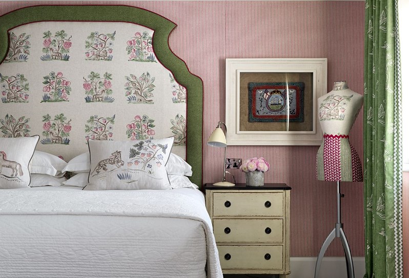 A spacious bedroom with a pink striped walls, a large king sized bed with a cream patterned headboard with a green trim