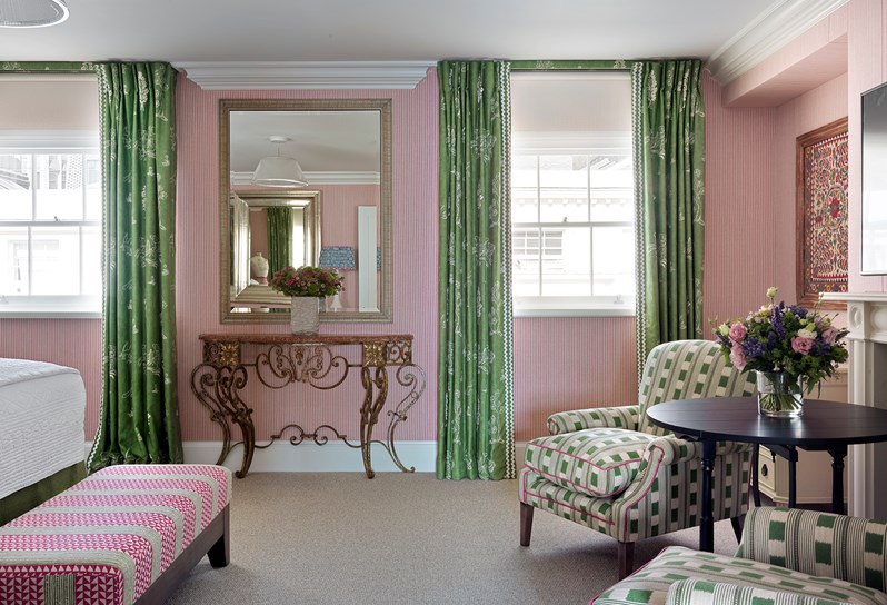 A spacious bedroom with a pink striped walls, and two large armchairs covered in a green fabric