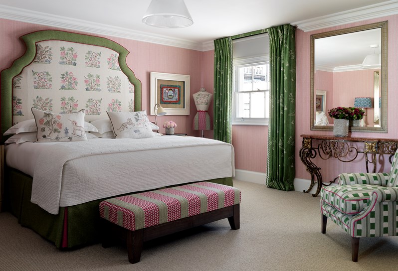 A spacious bedroom with a pink striped walls, a large king sized bed with a cream patterned headboard with a green trim