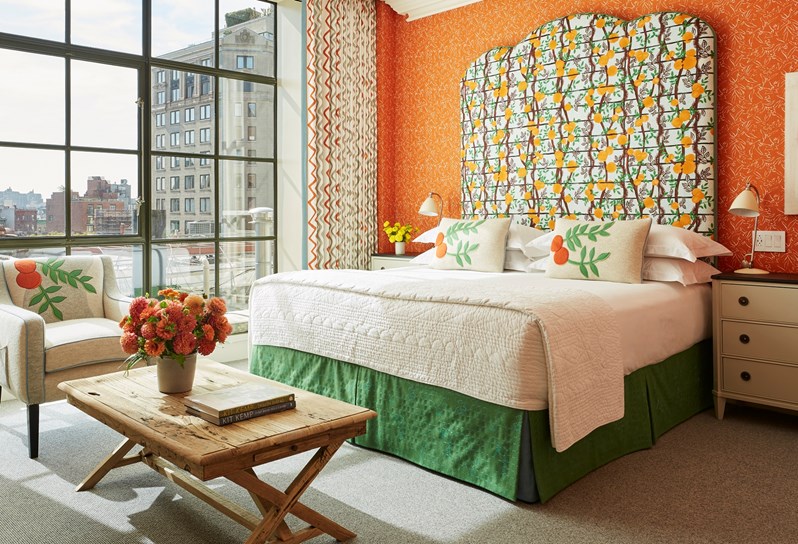 A colourful orange bedroom with a statement fabric headboard and floor to ceiling windows with views of New York