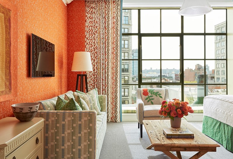 A colourful orange bedroom with a statement armchair and floor to ceiling windows with views of New York