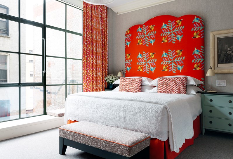 A grey room with a double bed with a bright red statement headboard
