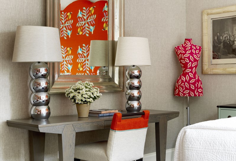 A sunny bedroom with cream walls and a small writing desk in front of a mirror
