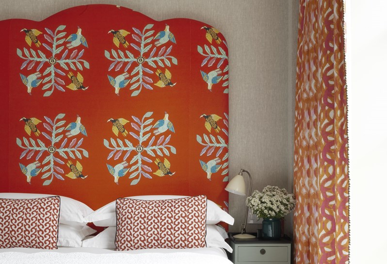 A sunny bedroom with a double bed with a red statement headboard.