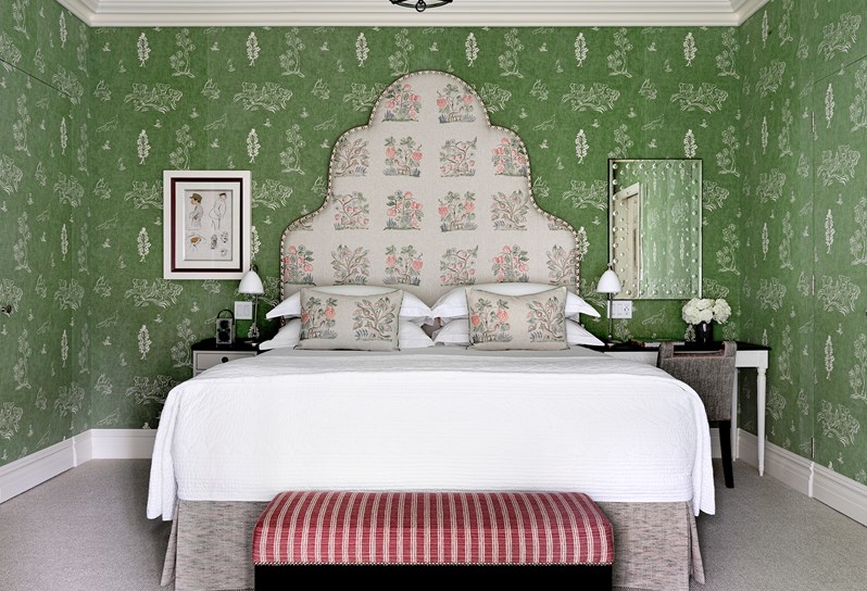 A bedroom with green patterned walls and a king size bed with a statement floral headboard