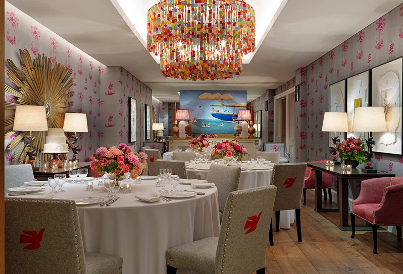 The Spring private dining room with blue walls and a multi-colored chandelier. The tables are set in rounds and decorated with beautiful flowers