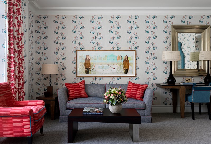 blue floral wallpaper and red sofa in the living room of a suite at The Soho Hotel