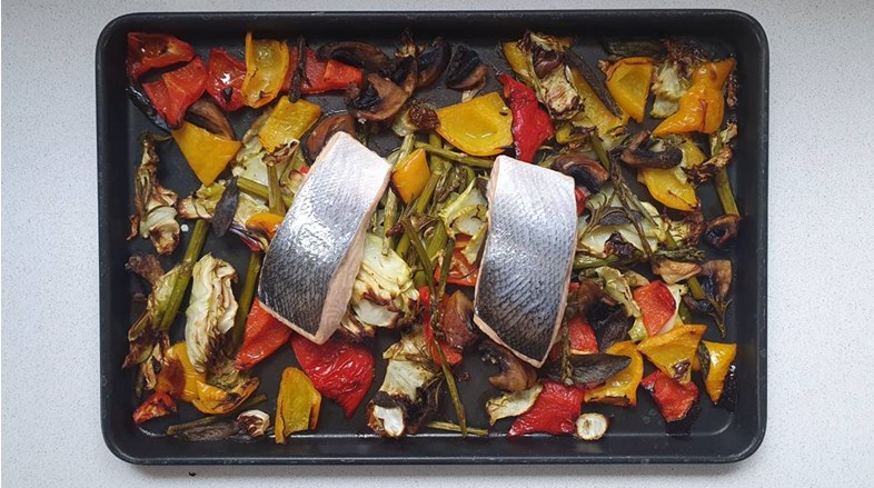 two portions of salmon on a bed of roasted vegetables in the pan