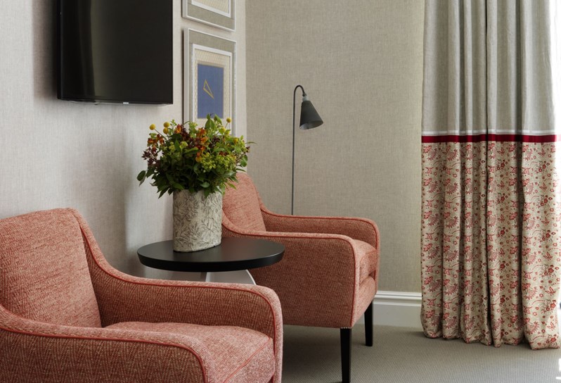 A bright sunny bedroom with cream walls and red chairs