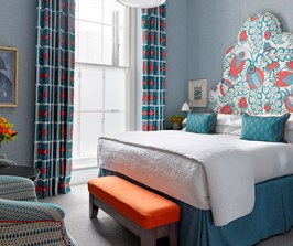 A bright sunny bedroom with blue walls and a large statement headboard covered in a bold red and blue fabric