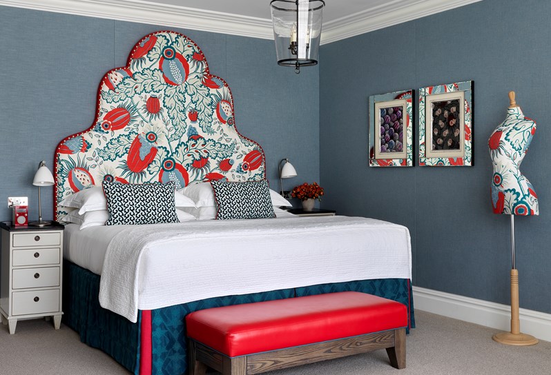 A spacious open plan suite containing a king sized bed with a floral headboard in red and blue colors and a matching mannequin