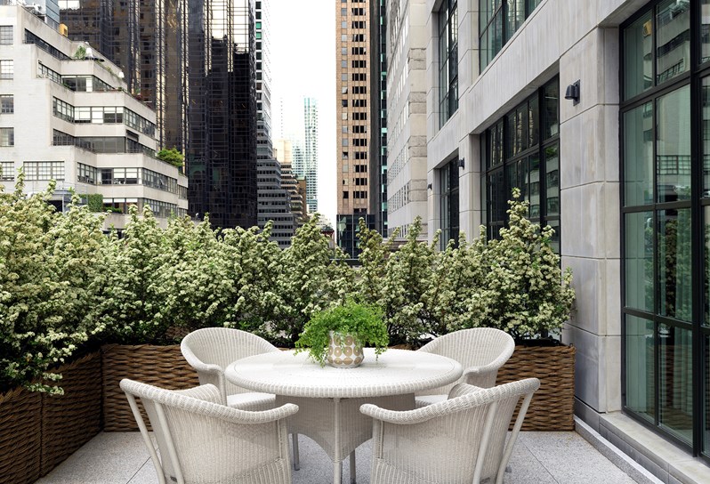 A leafy terrace overlooking Manhattan's skyline, containing comfortable patio furniture with dining space for four people.