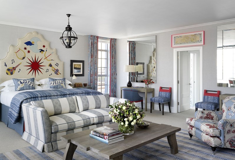 A bedroom which shows a bed, sofa, coffee table with design books and flowers, as well as a mirror and dressing table