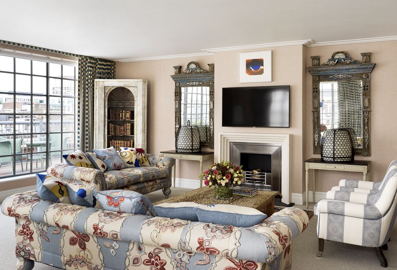 A living space with floral fabric sofas and a fireplace in the centre of the room.