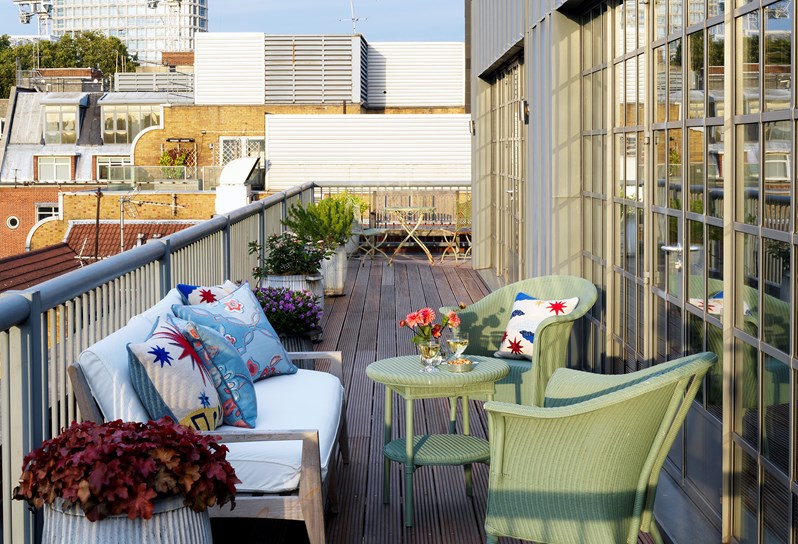 A private outdoor balcony at a hotel in Soho London with a sofa and table with chairs and loft style doors in the background.