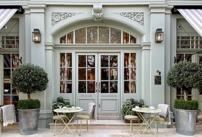 A terrace with green tables and chairs with grey blankets draped over the chair