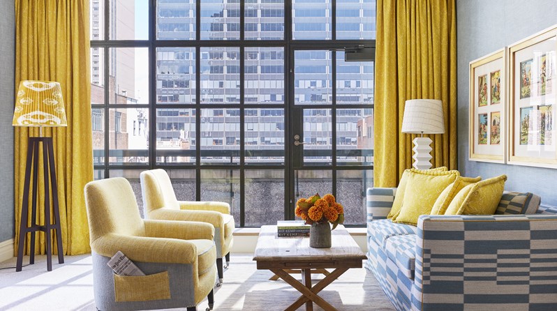 A bright yellow and blue sitting room of the corner terrace suite at The Whitby Hotel with sunlight flooding in through the floor to ceiling windows.