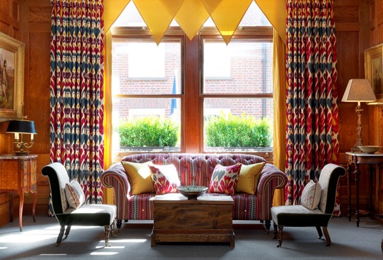 A sunny wood panelled drawing room with yellow curtains above a striped sofa