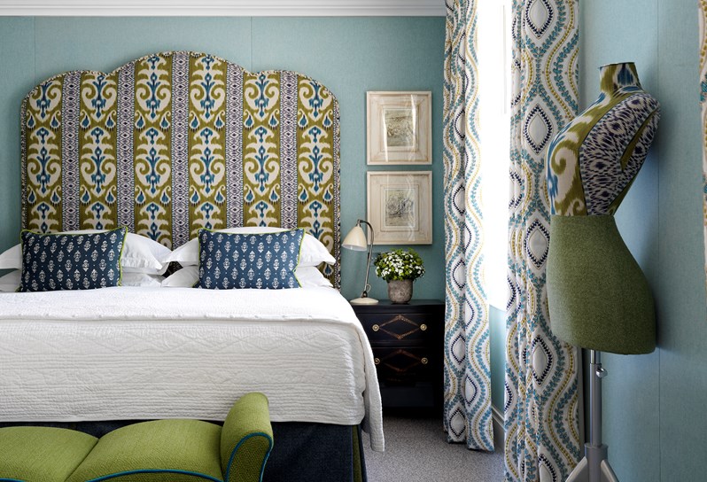 A spacious bedroom with bright blue walls and a king size bed with a blue and green fabric headboard