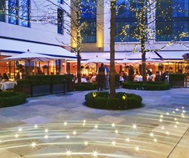 An open courtyard with lights in the trees, restaurant tables and twinkling lights on the flagstones
