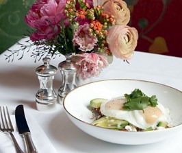 A brunch dish with two eggs next to an arrangement of colourful flowers.