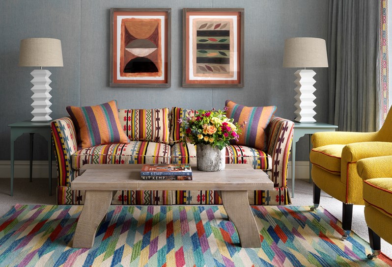 A colourful patterned sofa sitting against a blue linen wall. On the floor under a coffee table is a colourful rug.