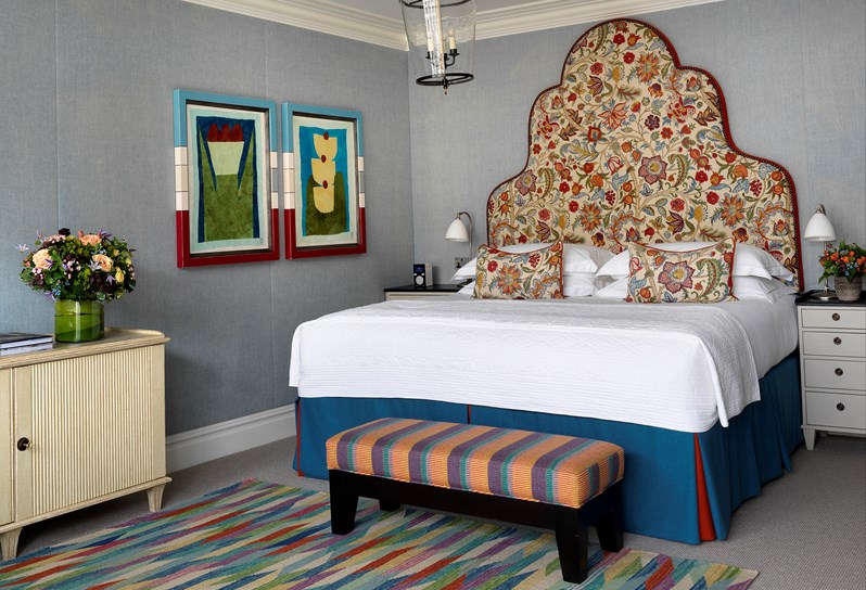 A large bed with a statement floral headboard. On the blue linen walls are two graphic paintings.