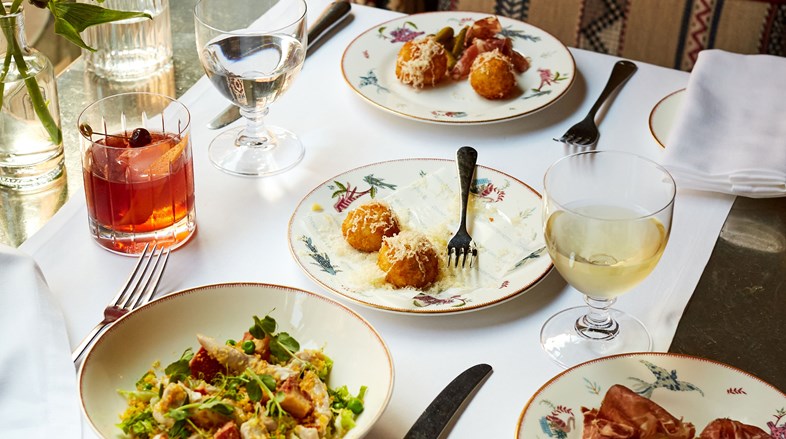 A table for two with plates of arancini, prosciutto and spring salads